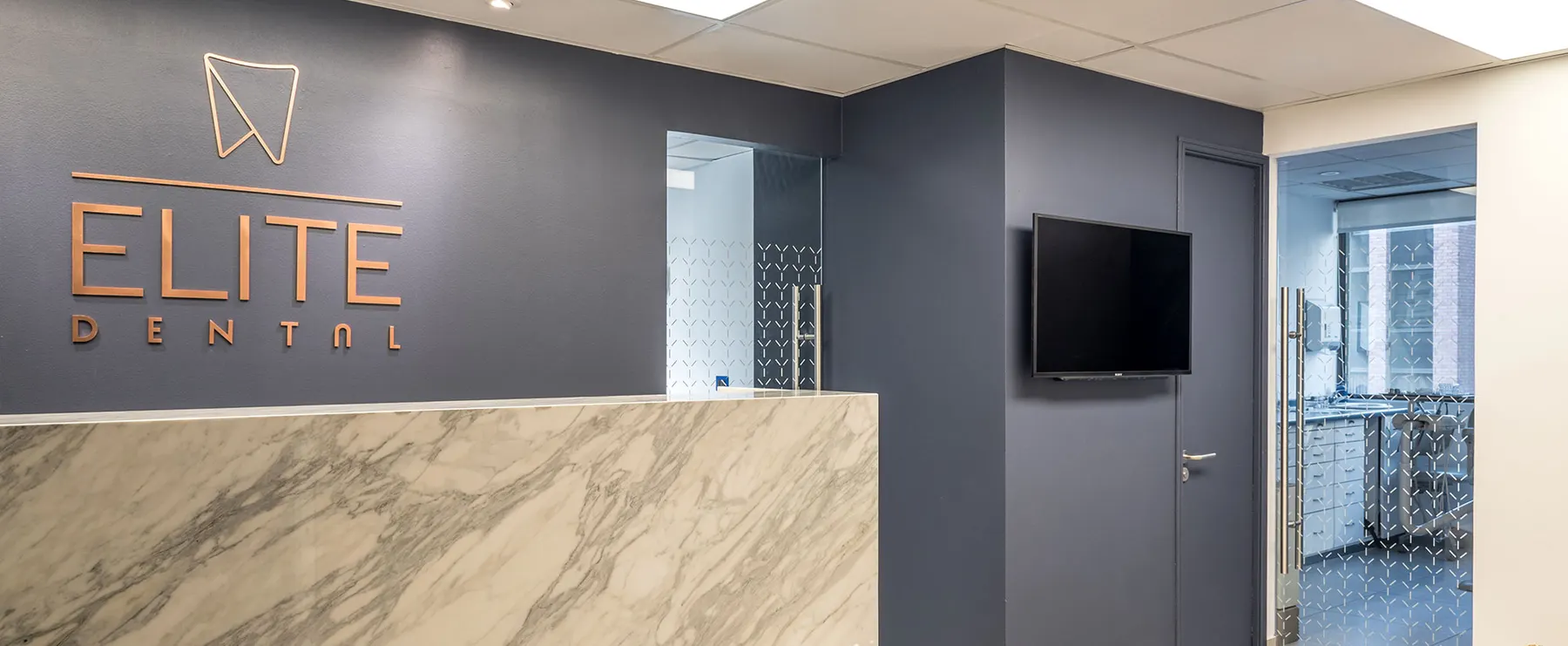 Recepción de Elite Dental en Providencia: logo cobre sobre muro azul y mesón de mármol blanco